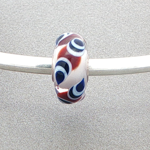 Brown, white and blue-black patterned murano glass bead on a silver bangle against a grey background