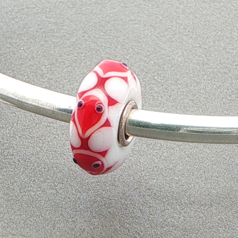 Red and white opaque glass bead with an animal face design on a silver bangle against a grey background