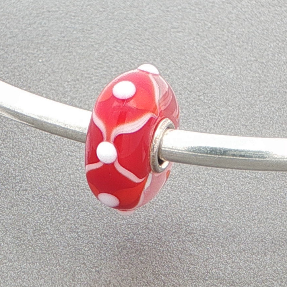 Silver bangle with a red and white glass bead against a gray background