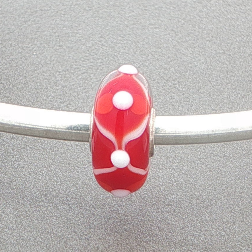 Red and white glass bead with white tactile dots on a silver bangle against a grey background