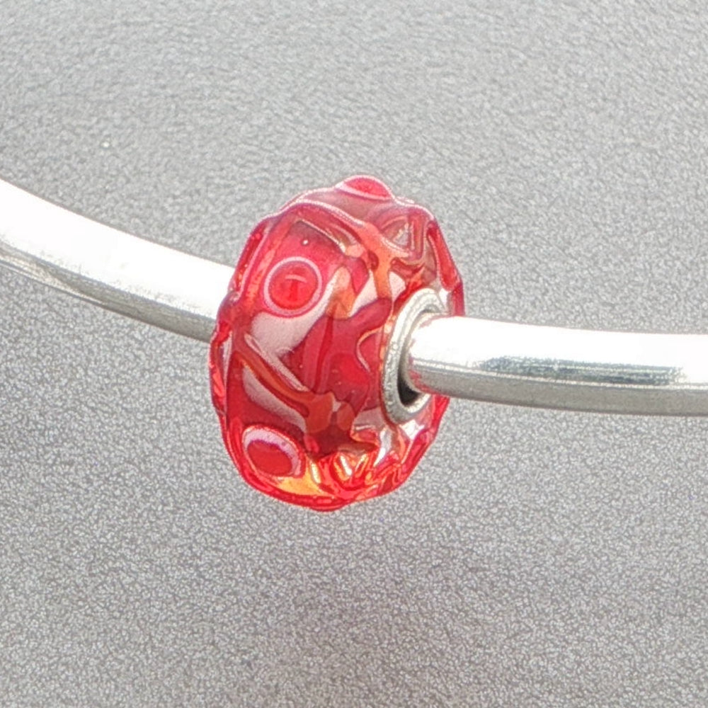 Red glass bead with a tactile design on a silver bangle against a grey background