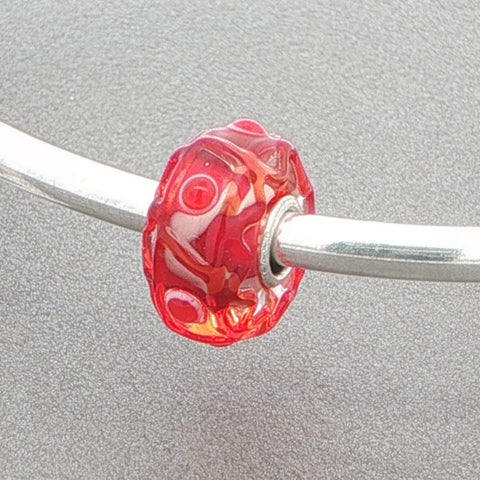 Red glass bead with a tactile design on a silver bangle against a grey background