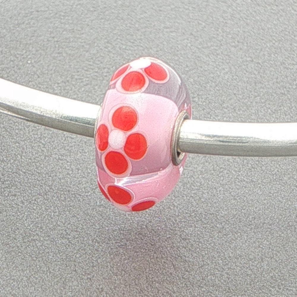 Pink bead with red floral designed bead on a silver metal bar against a gray background