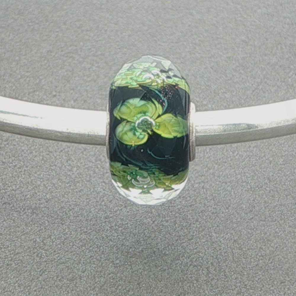 Faceted glass bead with green floral design and sprinkle of gold glitter on a grey background