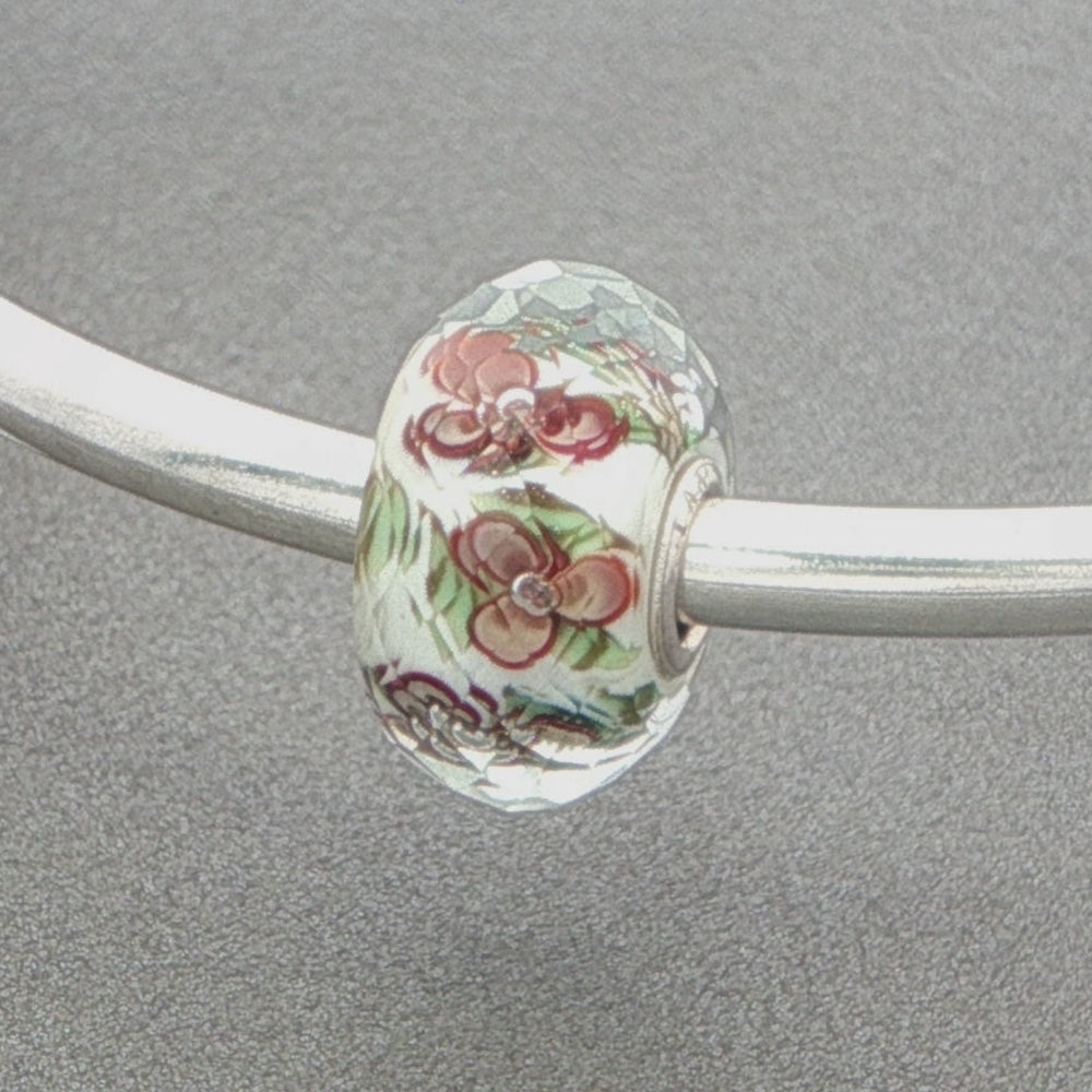 Floral glass faceted bead on a silver bangle against a grey background
