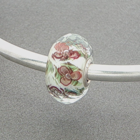 Floral glass faceted bead on a silver bangle against a grey background