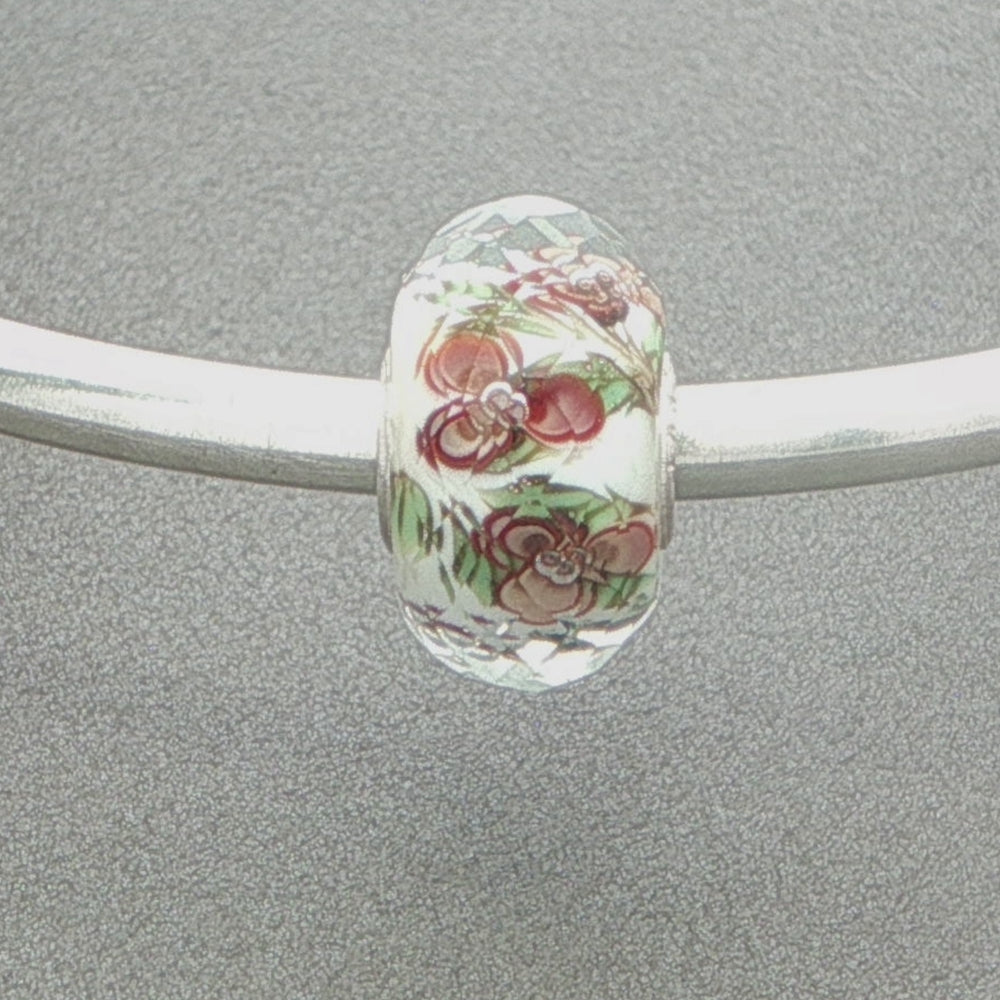 Decorative faceted glass bead with floral pattern on a silver bangle against a grey background