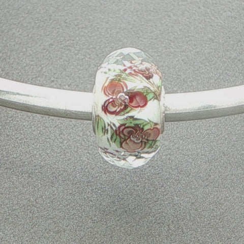 Decorative faceted glass bead with floral pattern on a silver bangle against a grey background