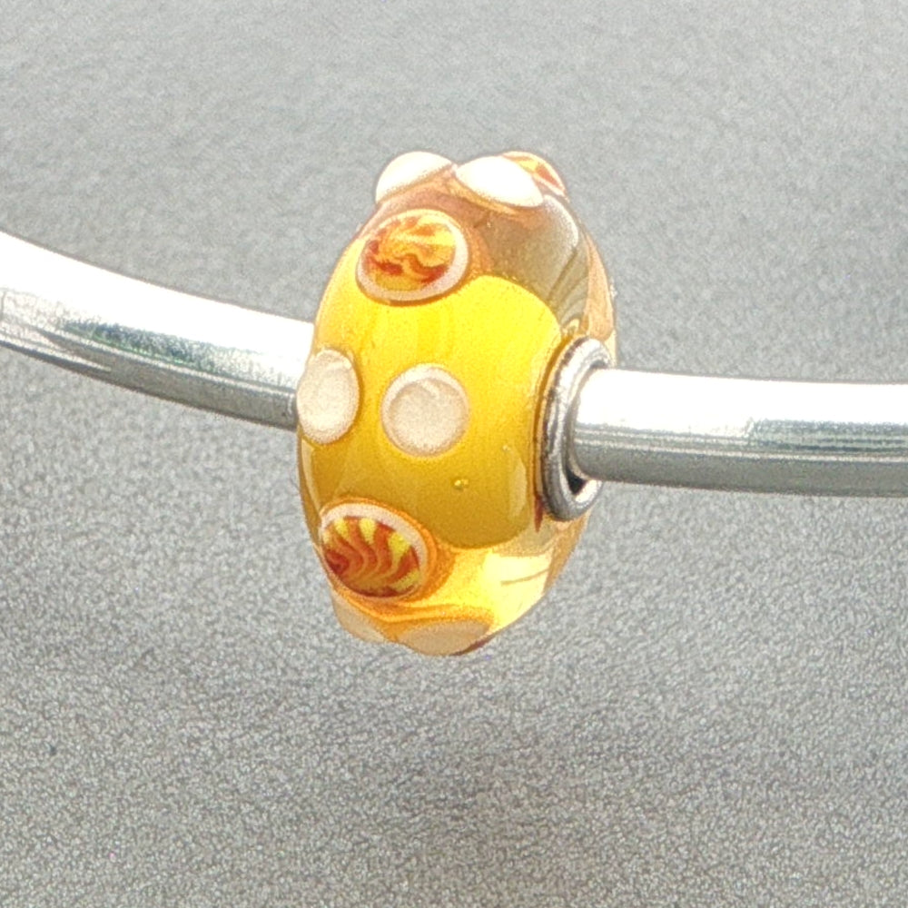 Yellow glass bead on a silver bangle against a grey background