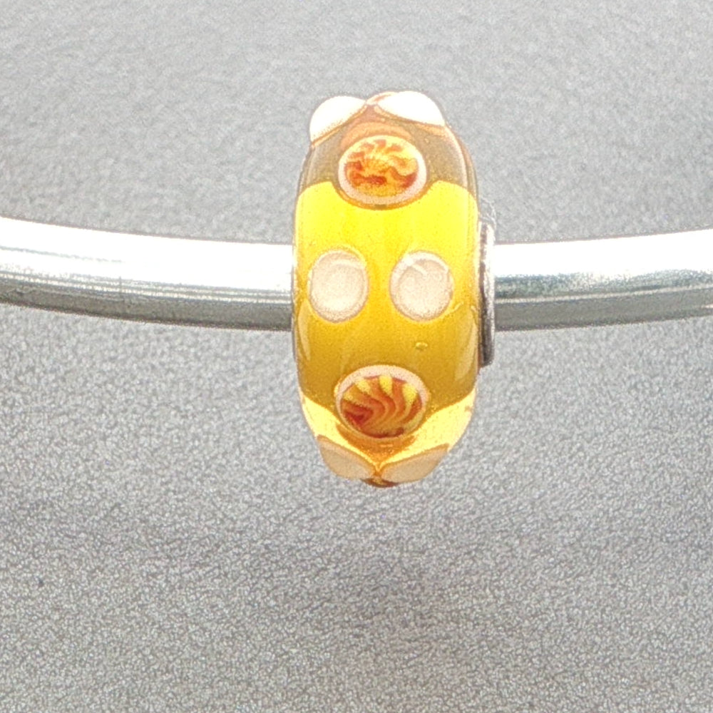 Yellow glass bead with swirl patterns and raised white dots on a silver bangle against a grey background