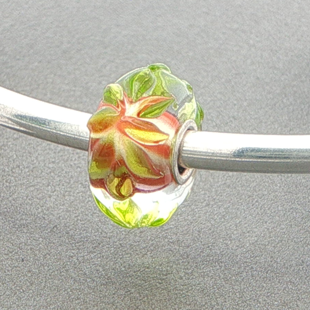 Glass bead with raised floral design on a silver bangle against a grey background