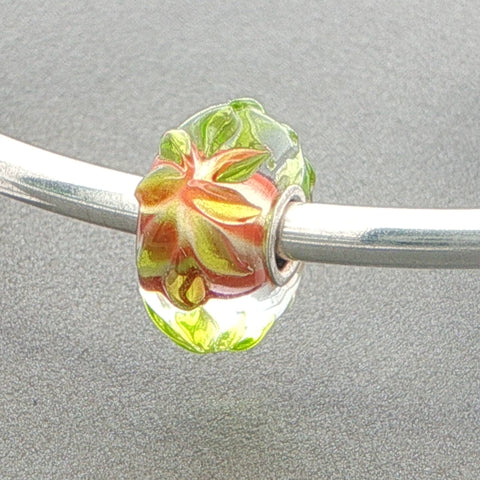 Glass bead with raised floral design on a silver bangle against a grey background