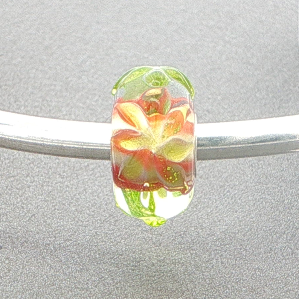 Glass bead with floral design on a silver bangle against a grey background