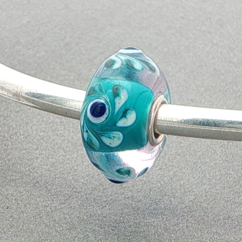 Turquoise glass bead on a silver bangle against a grey background
