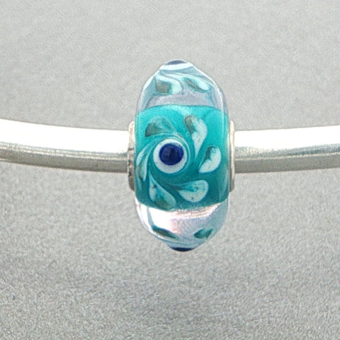 Turquoise glass bead with eye design on a silver bangle against a grey background