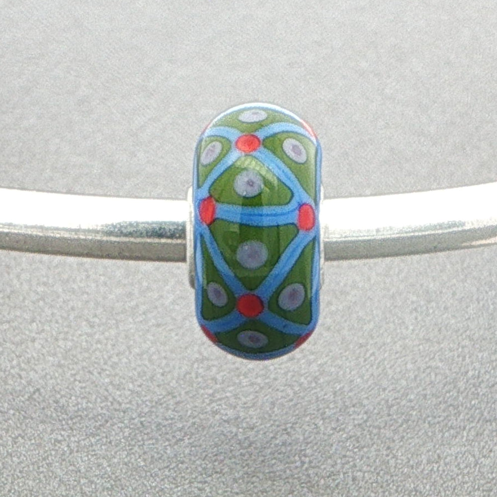 Decorative opaque bead with green and blue pattern on a silver bangle against a grey background