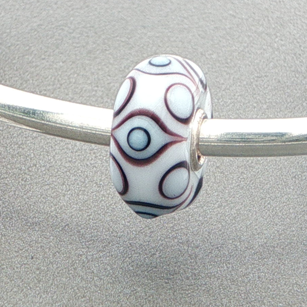 White opaque bead with an eye pattern on a silver bangle against a grey background