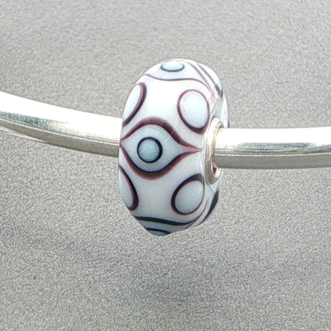 White opaque bead with an eye pattern on a silver bangle against a grey background