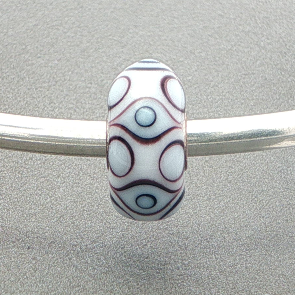 Decorative white opaque bead with eye design on a silver bangle against a grey background