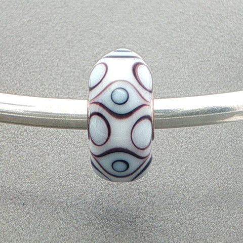 Decorative white opaque bead with eye design on a silver bangle against a grey background
