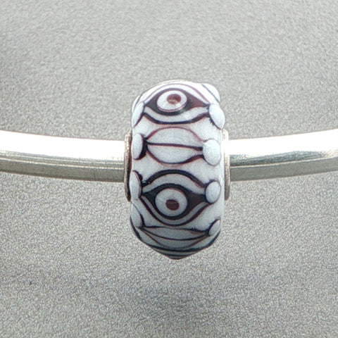 Decorative opaque white glass bead with eye pattern on a silver bangle against a grey background