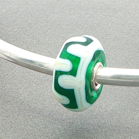 Green and white patterned glass bead on a silver bangle against a grey background