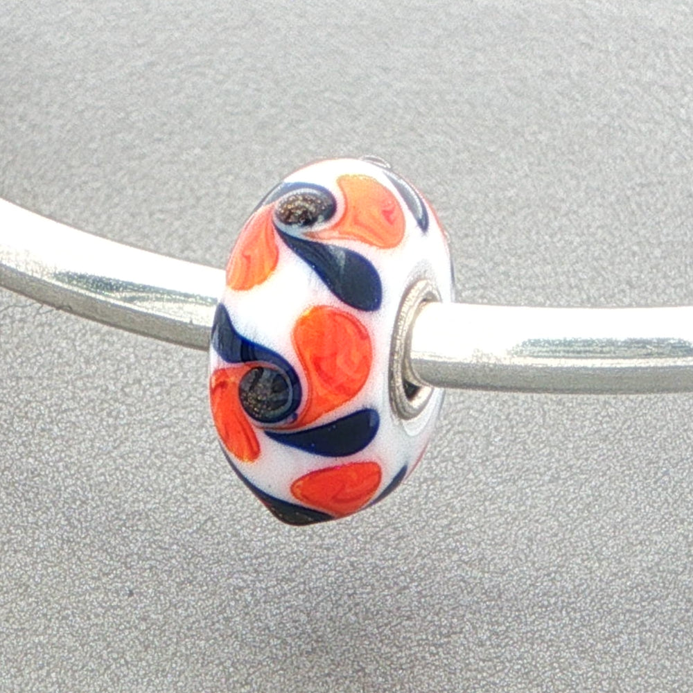 White opaque glass bead with orange and black pattern on a silver bangle against a grey background