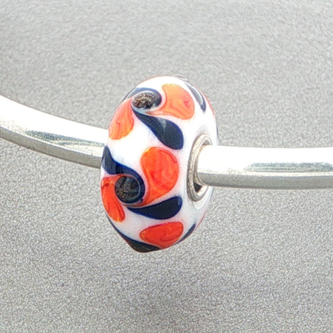 White opaque glass bead with orange and black pattern on a silver bangle against a grey background