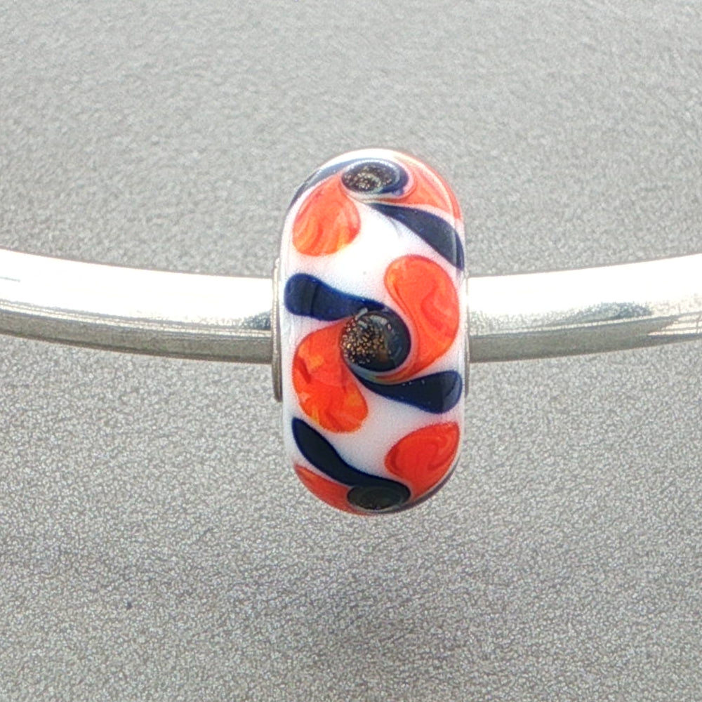 White opaque glass bead with black and orange swirls on a silver bangle against a grey background