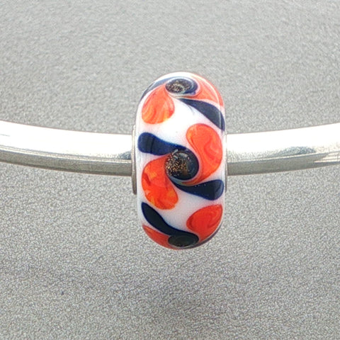 White opaque glass bead with black and orange swirls on a silver bangle against a grey background