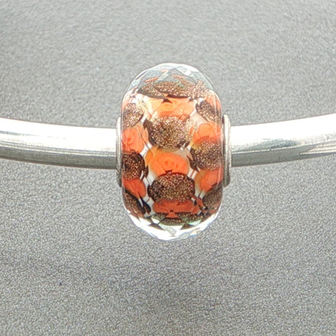Glass faceted bead with orange and brown pattern on a silver bangle against a grey background