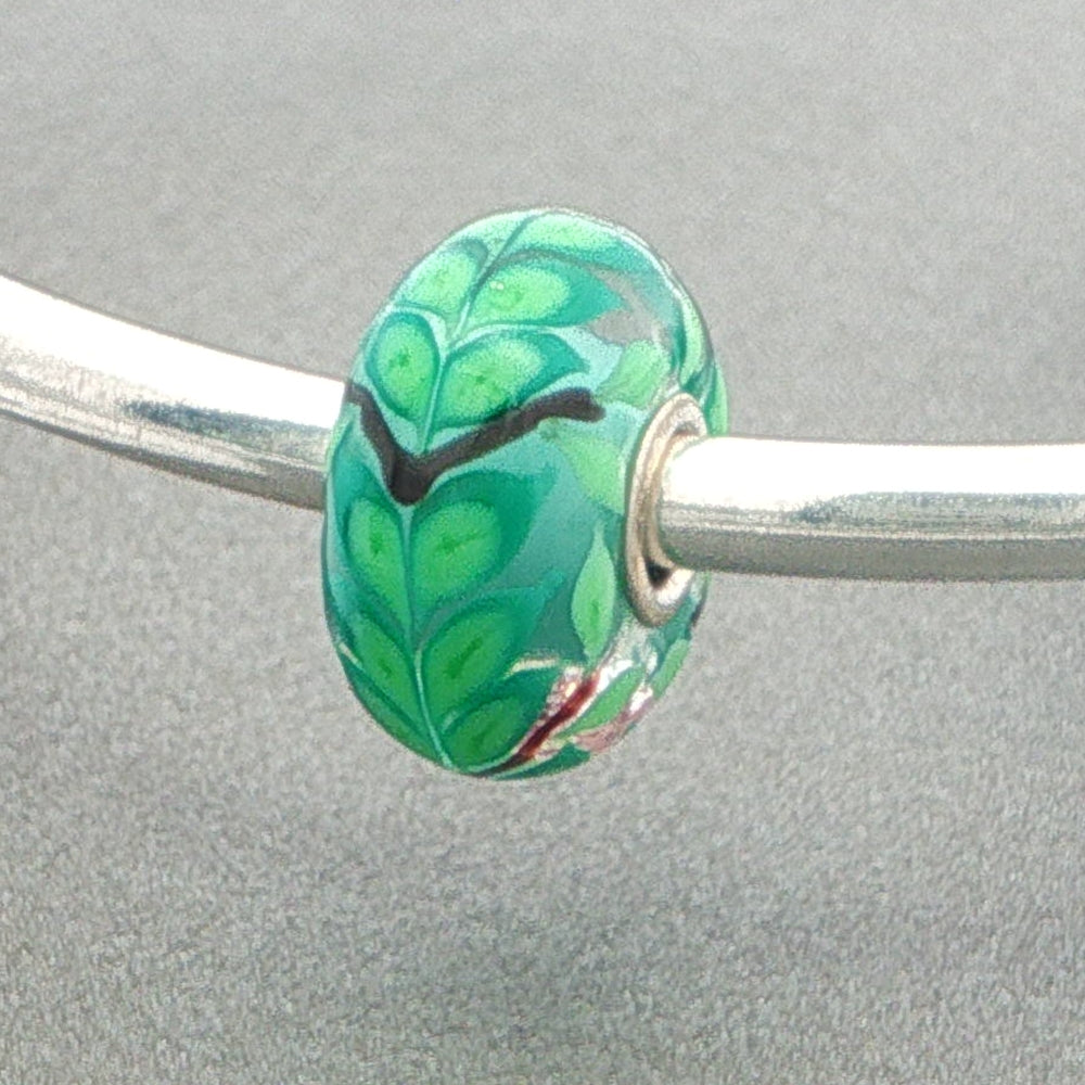 Green glass bead with leafy detail on a silver bangle against a grey background