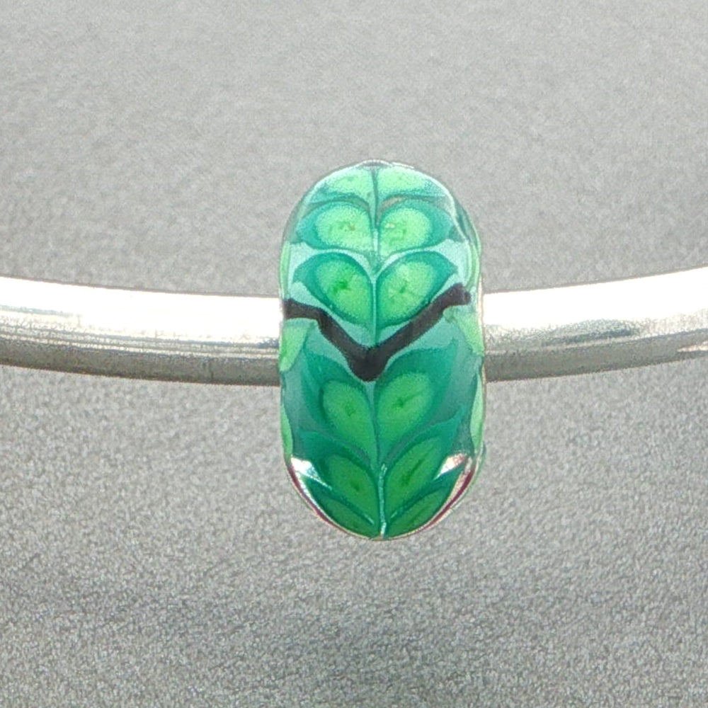 Green leafy patterned bead on a silver bangle against a grey background