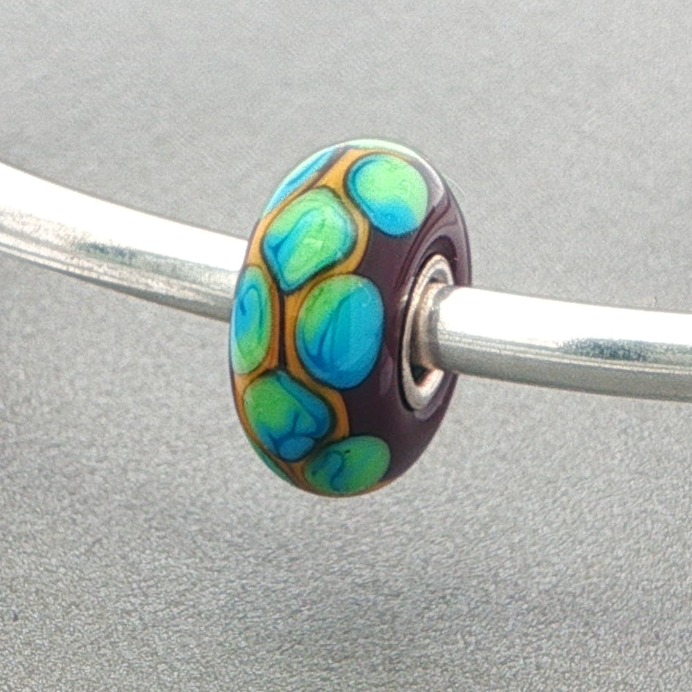 Multicolored glass bead on a silver bangle against a grey background