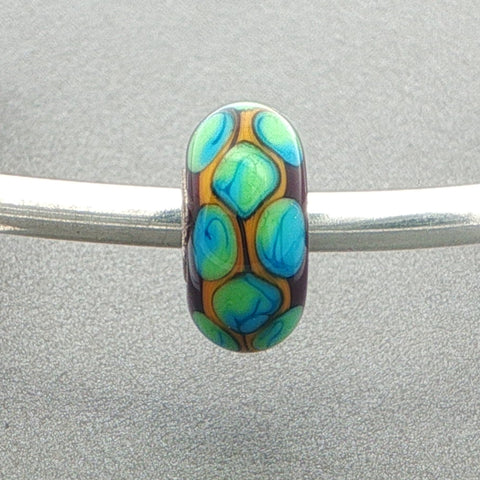 Decorative glass bead with blue and green pattern on a silver bangle against a grey background