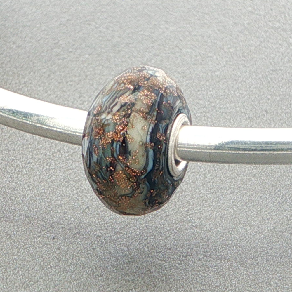 Decorative faceted glass bead on a silver bangle against a grey background