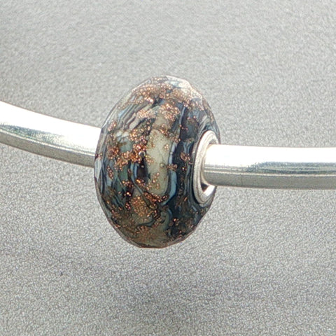 Decorative faceted glass bead on a silver bangle against a grey background