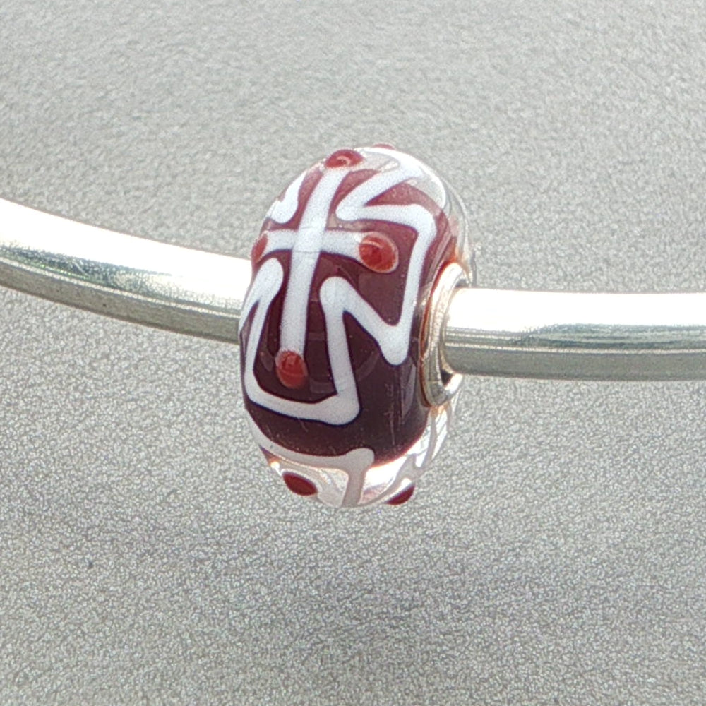 Glass bead with white cross pattern and red core on a silver bangle against a grey background