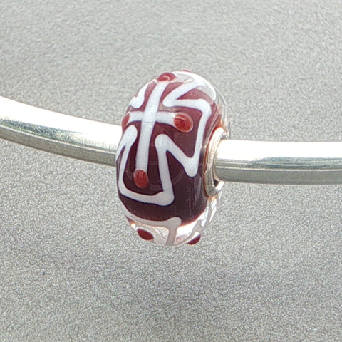 Glass bead with white cross pattern and red core on a silver bangle against a grey background