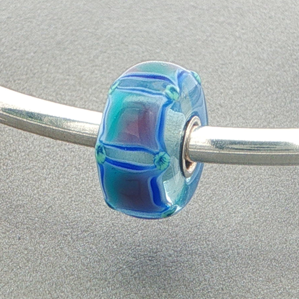 Blue Squares in a light blue glass bead on a silver bangle against a grey background
