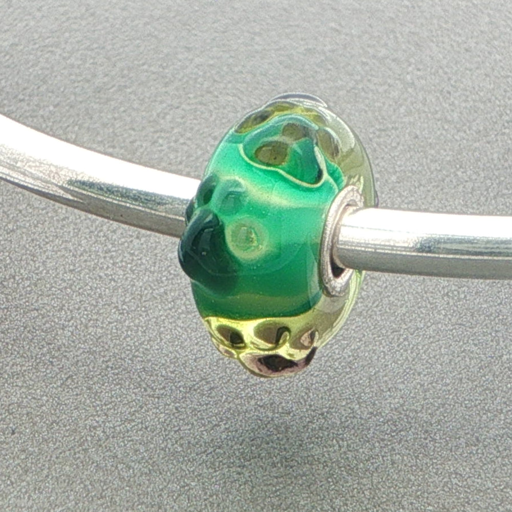 Green glass bead with tactile paw print design on a silver bangle against a grey background