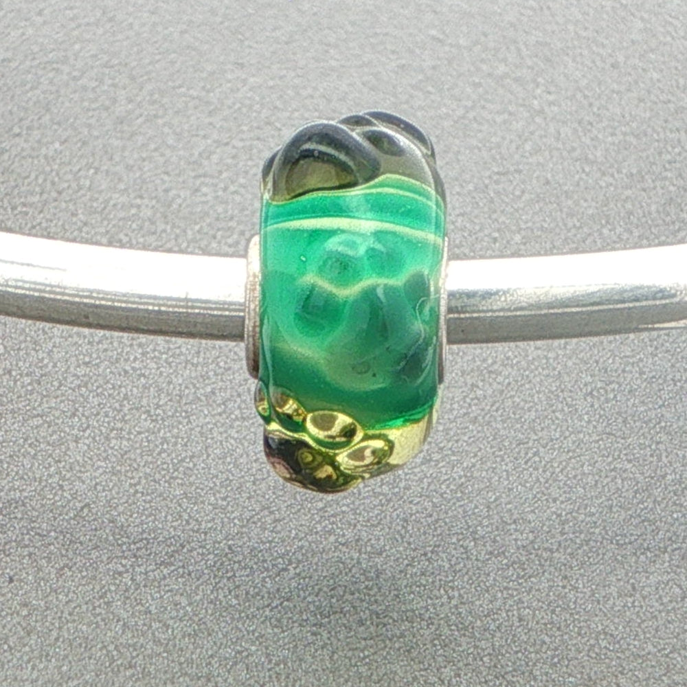 Green glass bead with tactile paw prints on a silver bangle against a grey background