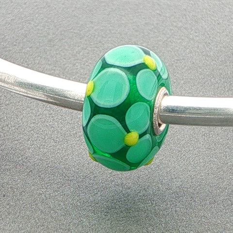 Green petal designed glass bead on a silver bangle against a grey background