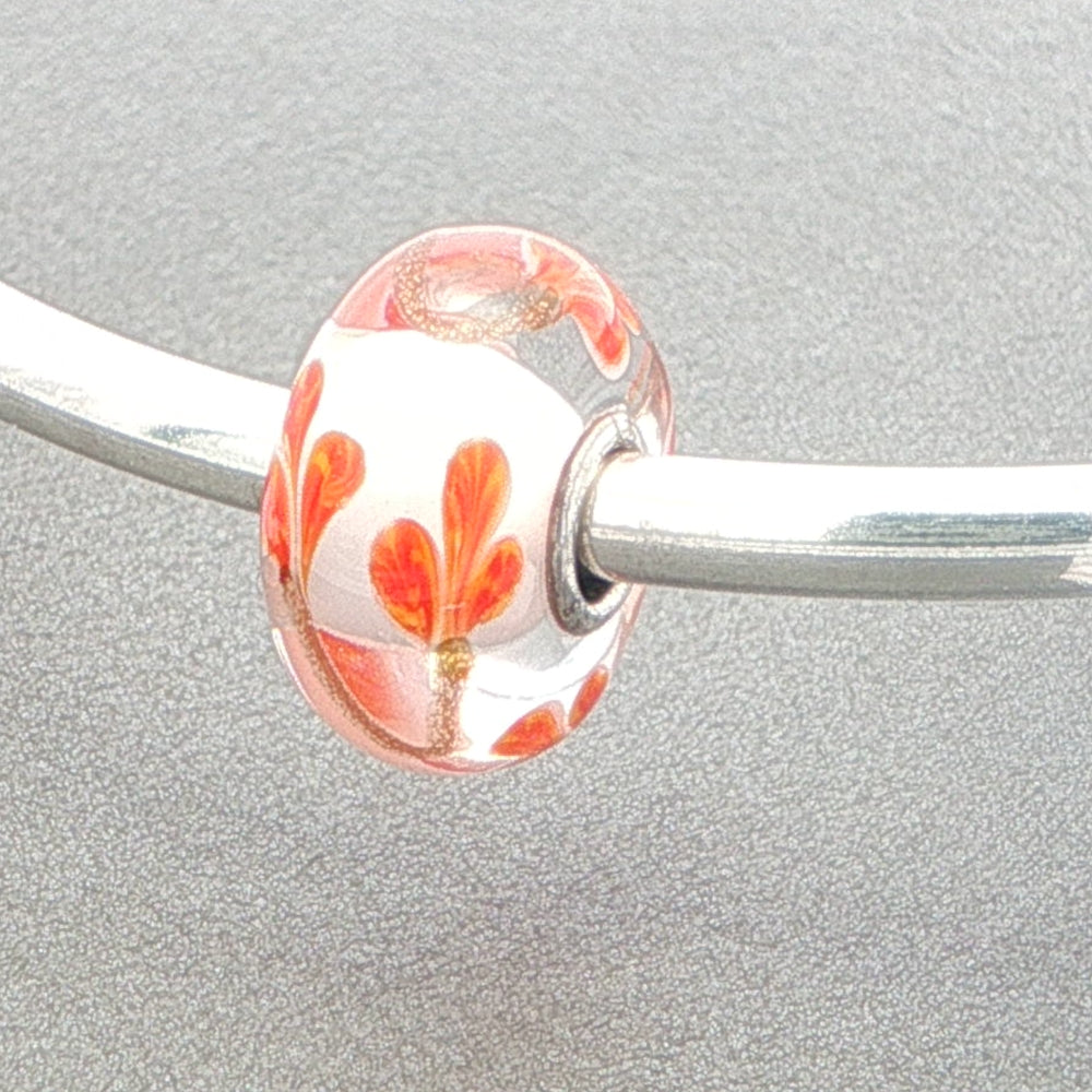 Orange petals and golden stem designed glass bead on a silver bangle against a grey background