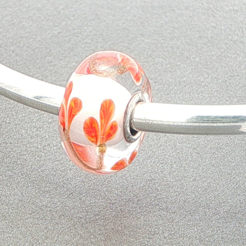 Orange petals and golden stem designed glass bead on a silver bangle against a grey background