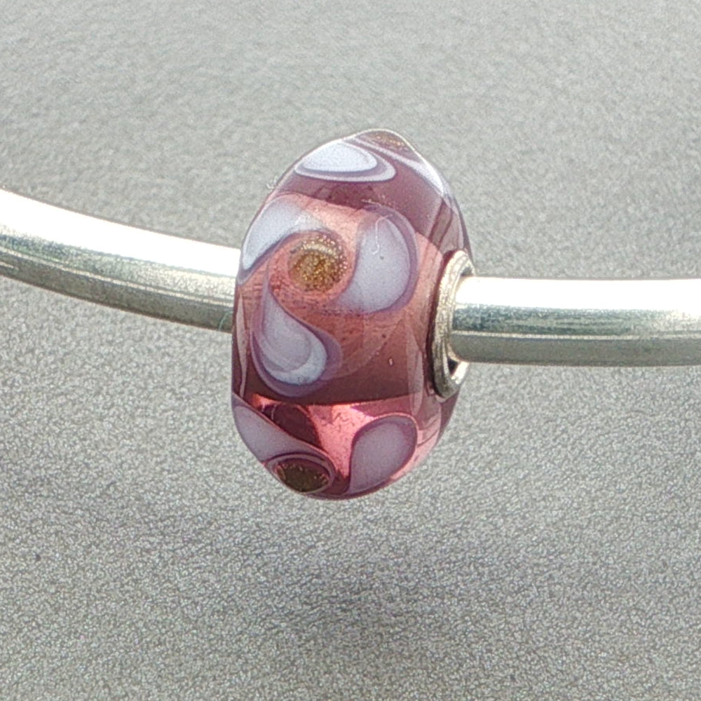 Mauve and white  decorated glass bead on a silver bangle against a grey background