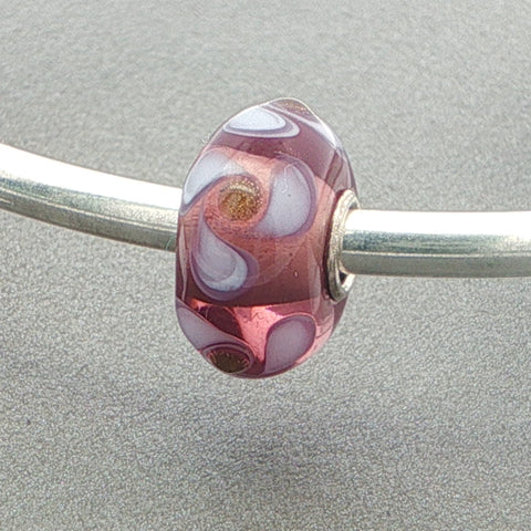 Mauve and white  decorated glass bead on a silver bangle against a grey background