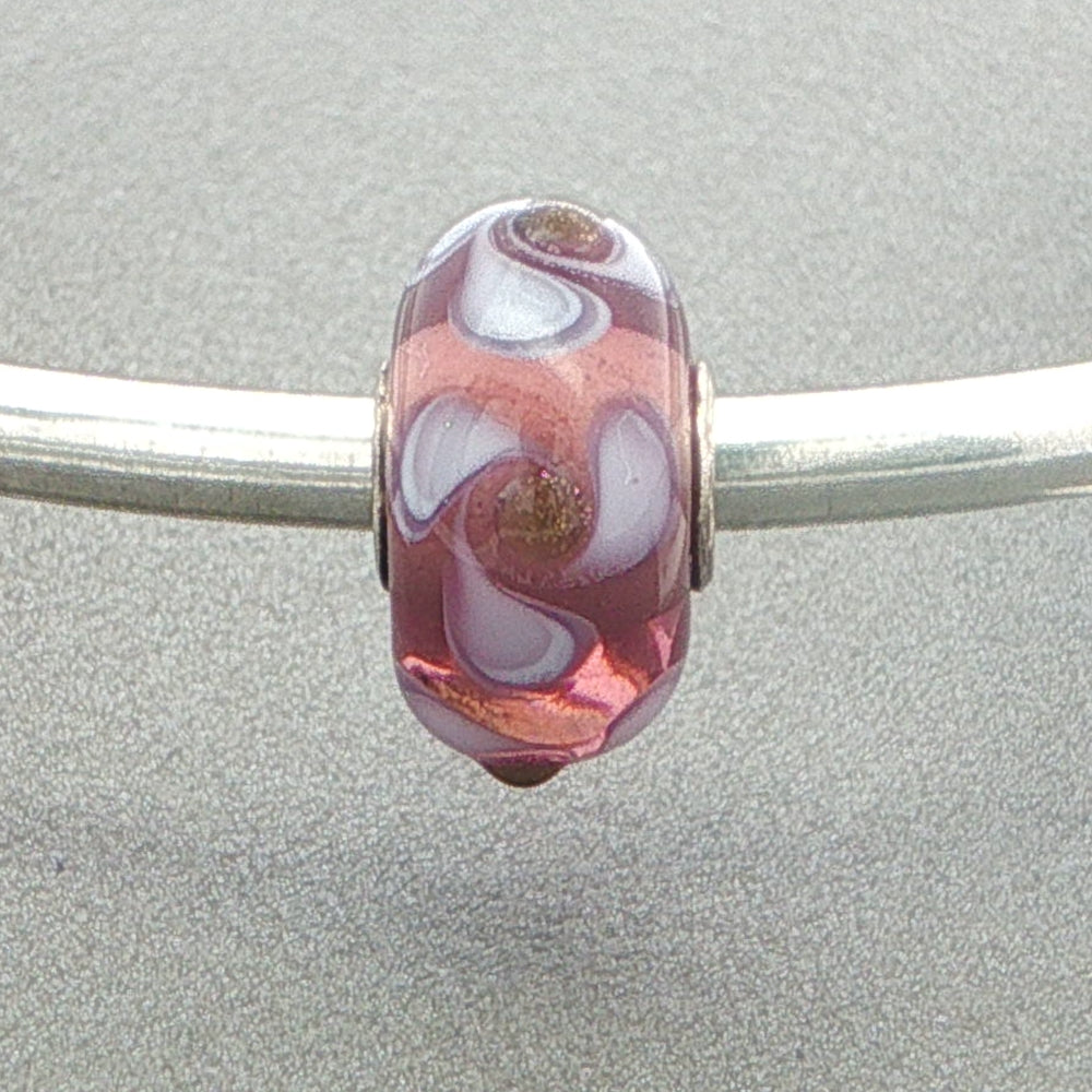 Mauve and white twirling petal patterned glass bead on a silver bangle against a grey background