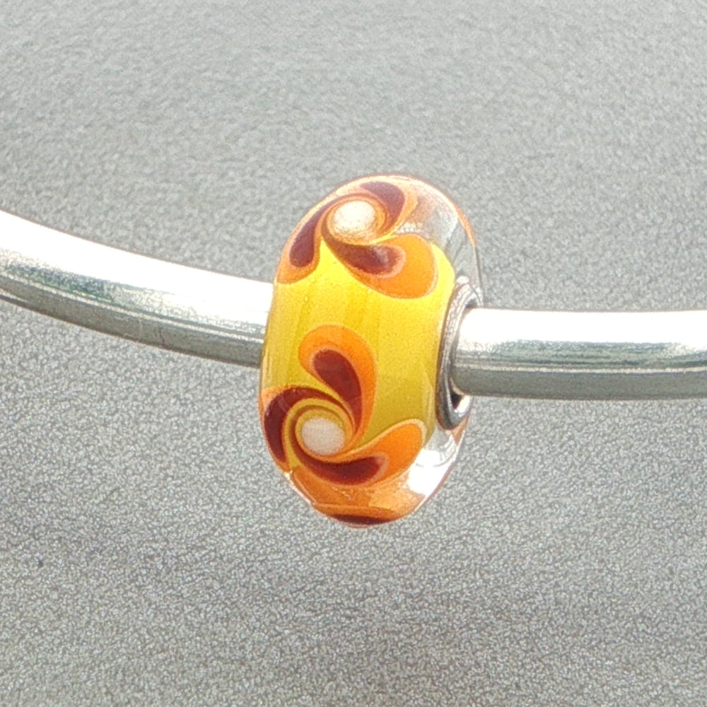Glass bead with orange and brown swirl design on a silver bangle against a grey background