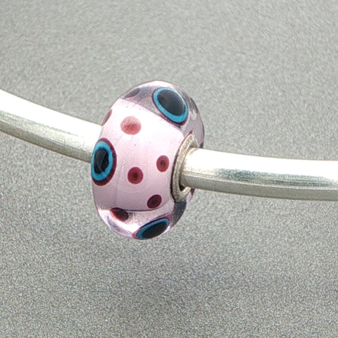 Decorative glass bead with burgundy and blue patterns on a silver bangle against a grey background